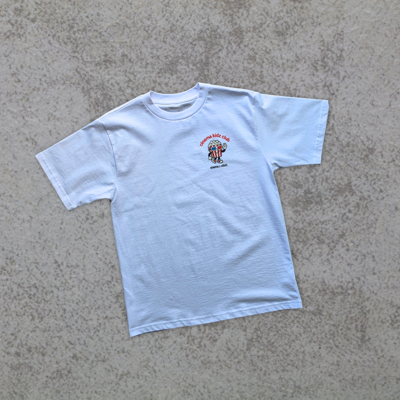 A light blue short-sleeve t-shirt with a small graphic on the left chest, laid flat on a textured gray concrete surface.