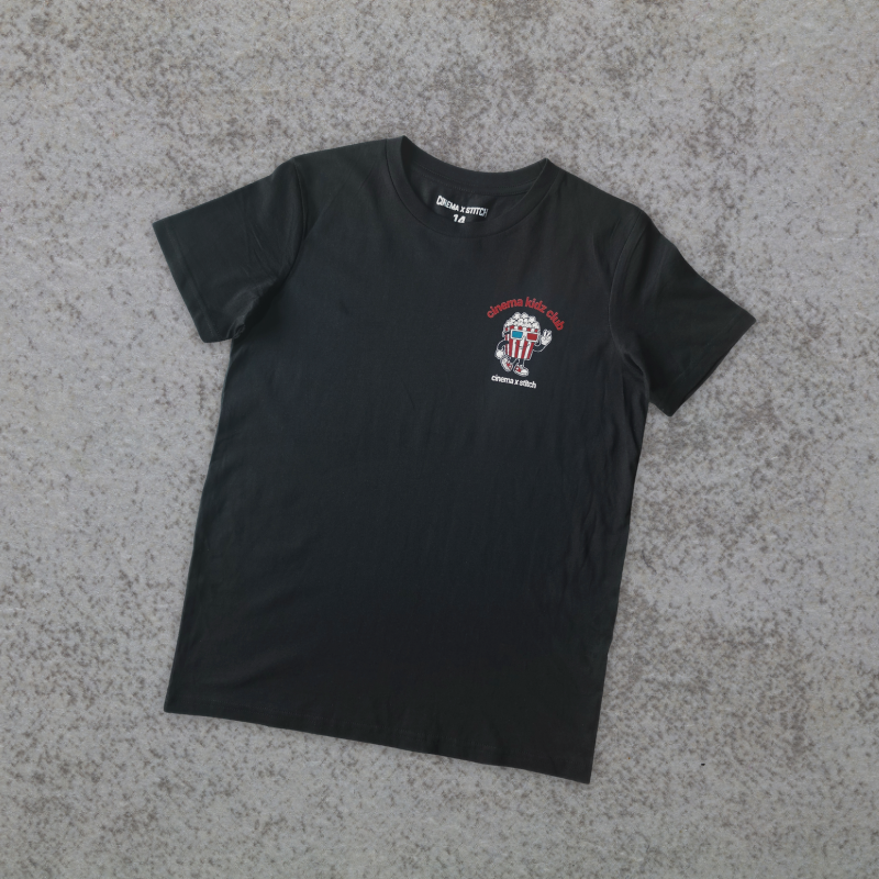 A black short-sleeve t-shirt with a small patriotic graphic on the left chest, laid flat on a textured gray surface.