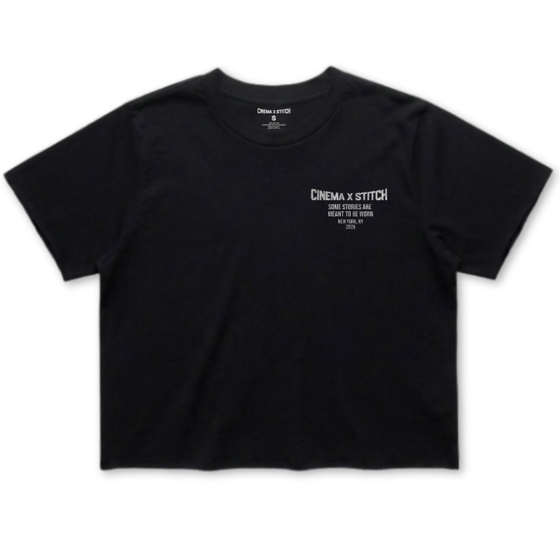 A black short-sleeve crop top t-shirt with white printed text on the left chest reading 'CINEMA X STITCH'.