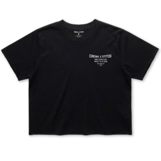 A black short-sleeve crop top t-shirt with white printed text on the left chest reading 'CINEMA X STITCH'.